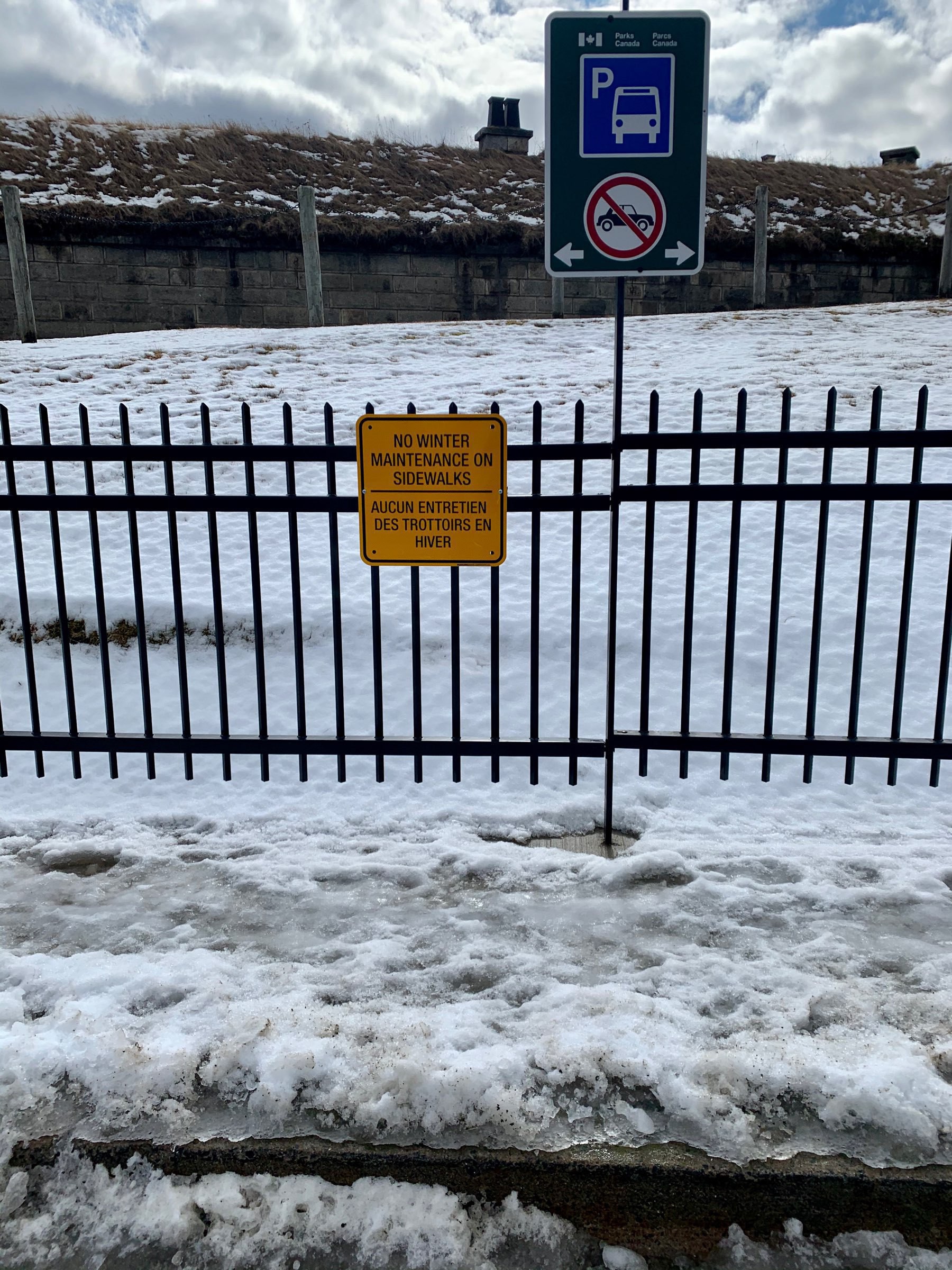 A snow-covered sidewalk next to a sign reading "No winter maintenance on sidewalks."